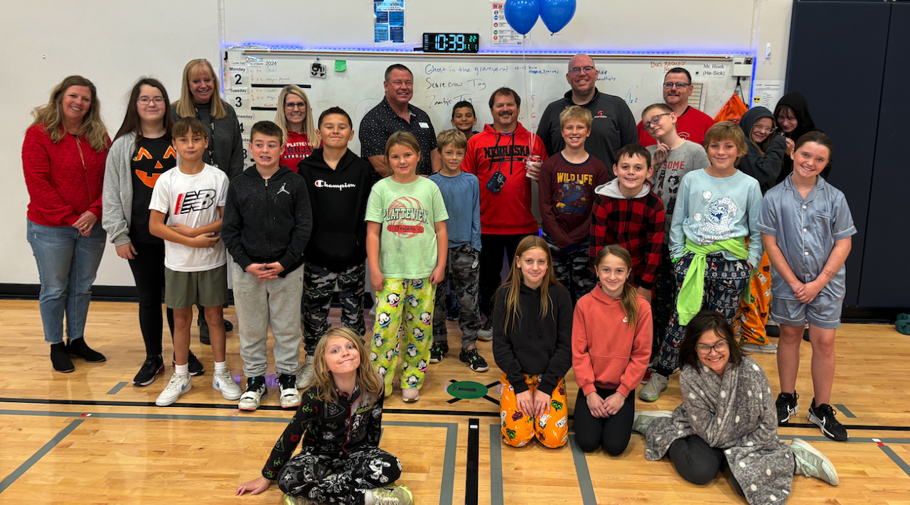 a classroom picture of children, a teacher and four administrators smiling at the camera celebrating the good vibes employee of the month.